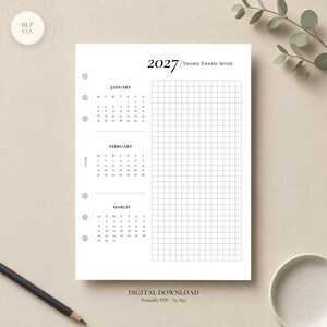 Puede incluir: Una hoja de agenda A5 blanca para el año 2027 con una cuadrícula a la derecha y calendarios mensuales de enero, febrero y marzo a la izquierda. La página incluye seis orificios circulares para encuadernación en el borde izquierdo y texto negro.