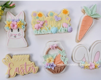 Pode incluir: Um conjunto de seis biscoitos de açúcar temáticos de Páscoa decorados com cores pastel e detalhes intrincados. Os biscoitos apresentam um coelho com uma coroa de flores, uma cena de jardim com um coelho, uma cenoura, uma cesta com cenouras e flores, e um letreiro de "Feliz Páscoa" com orelhas de coelho.