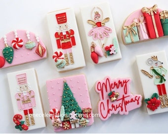 Puede incluir: Una variedad de galletas navideñas, que incluyen un cascanueces, una bailarina y un árbol de Navidad, decoradas con glaseado rojo, rosa, verde y dorado. Algunas galletas presentan el texto "Merry Christmas".