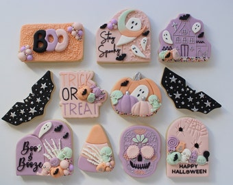 Pode incluir: Um conjunto de nove biscoitos temáticos de Halloween decorados com glacê roxo, rosa, laranja e preto. Os biscoitos apresentam vários desenhos, incluindo fantasmas, morcegos, abóboras, uma caveira, um milho doce, uma casa assombrada e as palavras "Boo & Booze", "Trick or Treat", "Stay Spooky" e "Happy Halloween".
