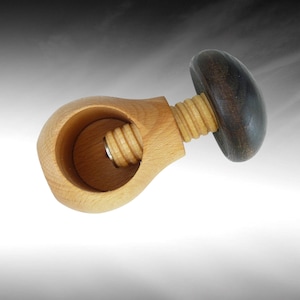 Op de afbeelding: Een houten notenkraker met een lichtbruine behuizing en een donkerbruine handgreep. De notenkraker heeft een schroefmechanisme. Het ontwerp is eenvoudig en functioneel, met een klassieke uitstraling.