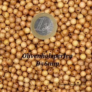 May include: A close-up image of a pile of small, round, light brown wooden beads. The beads have a hole in the center and are approximately 6 mm in diameter. The text "Olivenholzperlen D=6mm" is visible in the image.
