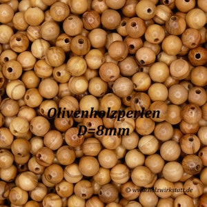 May include: A close-up image of a pile of natural wood beads. The beads are round and have a smooth, polished finish. The beads are approximately 8mm in diameter. The text "Olivenholzperlen D=8mm" is visible in the image.
