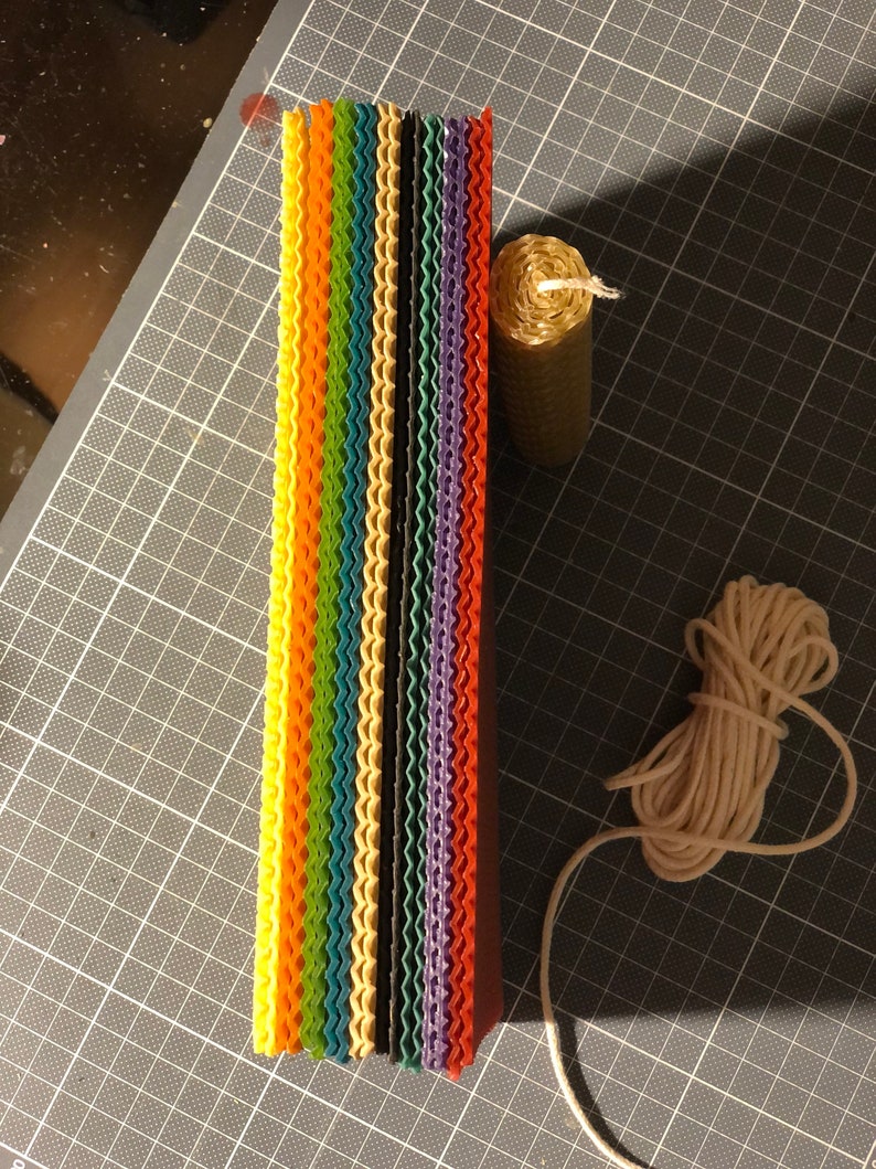 May include: A stack of colourful honeycomb wax sheets, a roll of beeswax, and a spool of white twine. These are materials for making candles.