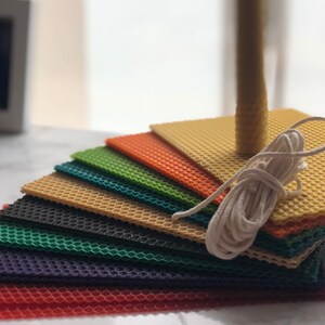 May include: A set of colourful honeycomb wax sheets for candle making. The sheets are stacked in a rainbow pattern, with a white wick and twine included.