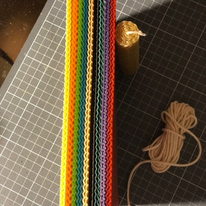 May include: A stack of colourful honeycomb wax sheets, a roll of beeswax, and a spool of white twine. These are materials for making candles.