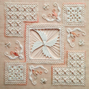 May include: Close-up of a handmade textile with intricate white and peach-colored lace designs. The piece features various square and floral patterns, with delicate bead accents. The background is a light peach fabric, showcasing the detailed needlework.