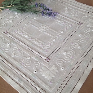 Peut inclure: Nappe brodée blanche avec un motif floral délicat et un motif central en forme de croix. La nappe est en lin fin et présente un bord festonné.