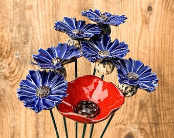 May include: A ceramic flower arrangement with a red poppy and blue cornflowers. The flowers are attached to green metal stems.