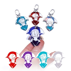 Puede incluir: Cinco llaveros de acrílico de colores con un personaje de dibujos animados con contornos blancos. Los llaveros tienen forma de flecha estilizada con un anillo de metal plateado.