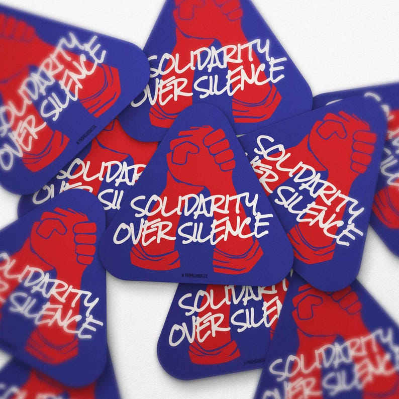 May include: A collection of blue, triangular stickers with the text "SOLIDARITY OVER SILENCE" in white. Each sticker features a red fist graphic. The stickers are scattered, creating a layered effect.