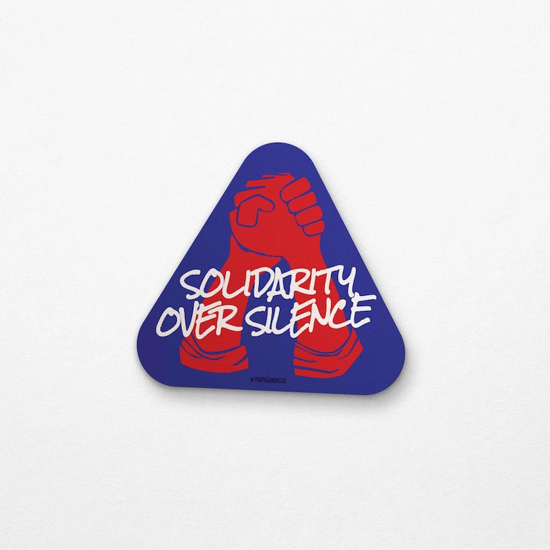 Triangle-shaped blue sticker featuring two red hands clasped in unity. White text reads "Solidarity Over Silence," inspired by the 1969 "Come Together in Peace" protest poster.