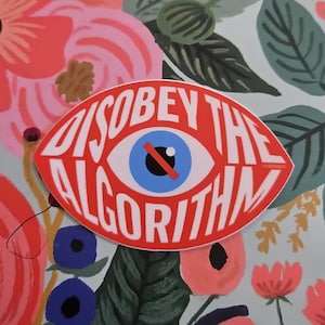 May include: A red, eye-shaped sticker with the words "DISOBEY THE ALGORITHM" in white. The eye has a blue iris, a black pupil, and a red line through it. The background features a floral pattern with pink and red flowers.