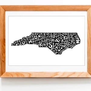 May include: A black and white typography art print of the state of North Carolina. The state outline is formed by the names of cities and towns in North Carolina, including Asheville, Charlotte, Raleigh, and Durham.