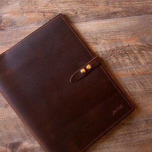 May include: A brown leather folder with a gold clasp and the text "Jim Cole" embossed on the front.