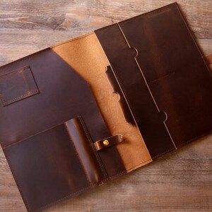 May include: A brown leather portfolio with multiple pockets and a flap closure. The portfolio is open and the inside is lined with a tan fabric.