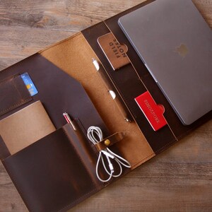 May include: A brown leather portfolio with a laptop, notebook, pens, and other accessories. The portfolio has multiple pockets and compartments for organization.
