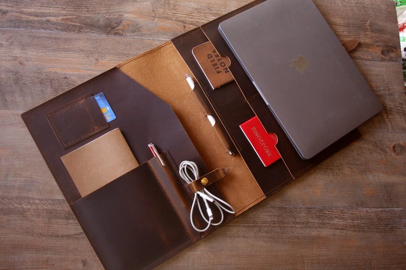 May include: A brown leather portfolio with a laptop, notebook, pens, and other accessories. The portfolio has multiple pockets and compartments for organization.