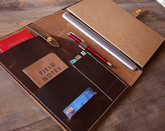 May include: A brown leather portfolio with multiple pockets and slots for carrying a passport, notebook, pens, and cards. The portfolio is open and the interior is lined with a brown fabric.