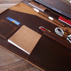 May include: A brown leather portfolio with multiple pockets and slots for carrying a laptop, pens, a notebook, and other accessories.