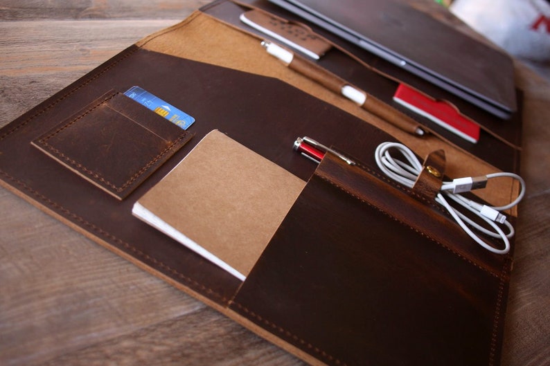 May include: A brown leather portfolio with multiple pockets and slots for carrying a laptop, pens, a notebook, and other accessories.