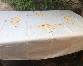 Könnte beinhalten: Weiße Tischdecke mit einem zarten Blumenmuster aus gelben Blüten und grünen Blättern. Die Tischdecke liegt auf einem Tisch und hat einen leicht zerknitterten Look.