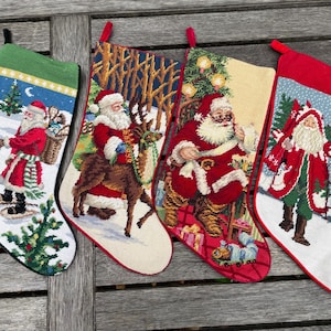 Puede incluir: Cuatro calcetines navideños con diseños festivos de Papá Noel. Cada calcetín presenta una escena diferente, incluyendo a Papá Noel con una linterna, montando un reno, leyendo una lista y llevando regalos. Los calcetines tienen detalles en rojo, verde y blanco.