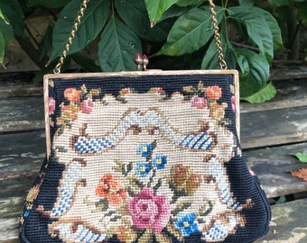 以下が含まれることがあります： ゴールドチェーンストラップと花柄の刺繍デザインが施されたヴィンテージの黒いハンドバッグ。刺繍は、クリーム色の背景にピンク、ブルー、オレンジの花が施されています。