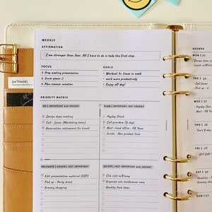May include: A weekly planner with a brown leather cover and gold rings. The planner has a white interior with a section for weekly affirmations, goals, focus, and a priority matrix. The priority matrix is divided into four quadrants: Do Important and Urgent, Plan Important, Not Urgent, Delegate Urgent, Not Important, and Delete Not Important and Urgent. The planner also has a section for a daily agenda.