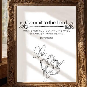 Può includere: Una stampa incorniciata con il testo "Commit to the Lord" e il versetto biblico Proverbi 16:3. La stampa presenta un motivo floreale e una farfalla. La cornice è ornata e dorata, e la stampa è esposta su un pavimento in legno.
