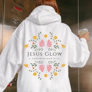 May include: White hoodie with a floral design and the text "JESUS GLOW 2 CORINTHIANS 5:17" printed on the back.