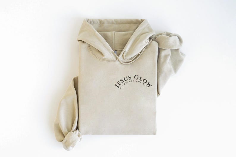 May include: A beige hoodie with the text "JESUS GLOW 2 CORINTHIANS 1:20" printed on the front.
