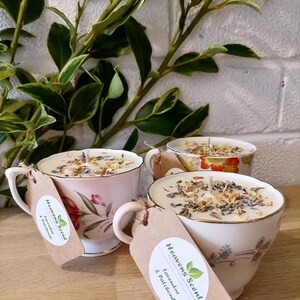 May include: Three vintage teacups filled with soy wax candles. The candles are topped with dried lavender and flowers. The teacups are decorated with floral patterns. The candles are labeled "Heavens Scent" with the scents "Lavender & Patchouli" and "Eucalyptus & Peppermint".
