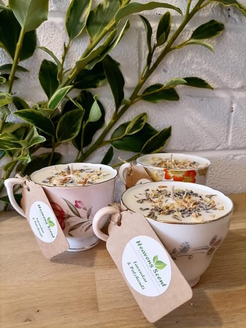 May include: Three vintage teacups filled with soy wax candles. The candles are topped with dried lavender and flowers. The teacups are decorated with floral patterns. The candles are labeled "Heavens Scent" with the scents "Lavender & Patchouli" and "Eucalyptus & Peppermint".