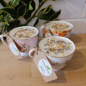 May include: Three teacup candles with floral designs and dried flowers on top. The candles are labeled "Heaven Scent" and "Lavender & Patchouli".