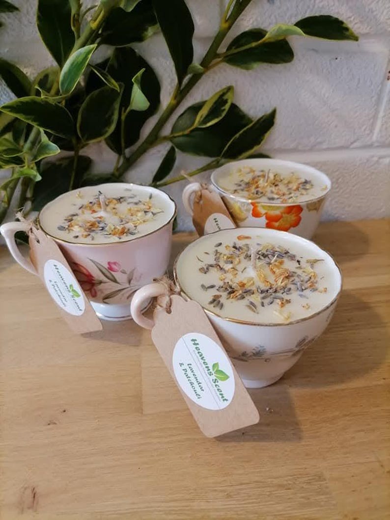 May include: Three teacup candles with floral designs and dried flowers on top. The candles are labeled "Heaven Scent" and "Lavender & Patchouli".