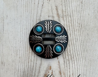 May include: Black metal buckle with a silver design and turquoise stones. The buckle has a rectangular opening in the center.