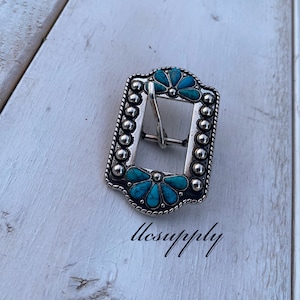 May include: Silver belt buckle with a turquoise flower design.