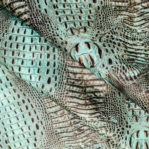 May include: Close-up of a textured, teal-colored alligator skin. The skin has a pattern of scales and pores, creating a unique and luxurious look.