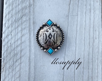 May include: Silver and turquoise concho with an eagle design. The concho has a decorative border and two turquoise stones.
