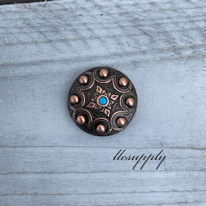 May include: A round, copper-colored metal button with a turquoise stone in the center. The button has a starburst design with six points and six raised circles around the edge.