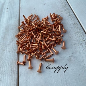 May include: A large pile of copper-colored metal rivets on a white wooden surface. The rivets are about 1/2 inch long and have a flat head. The text "llcsupply" is visible in the lower right corner of the image.