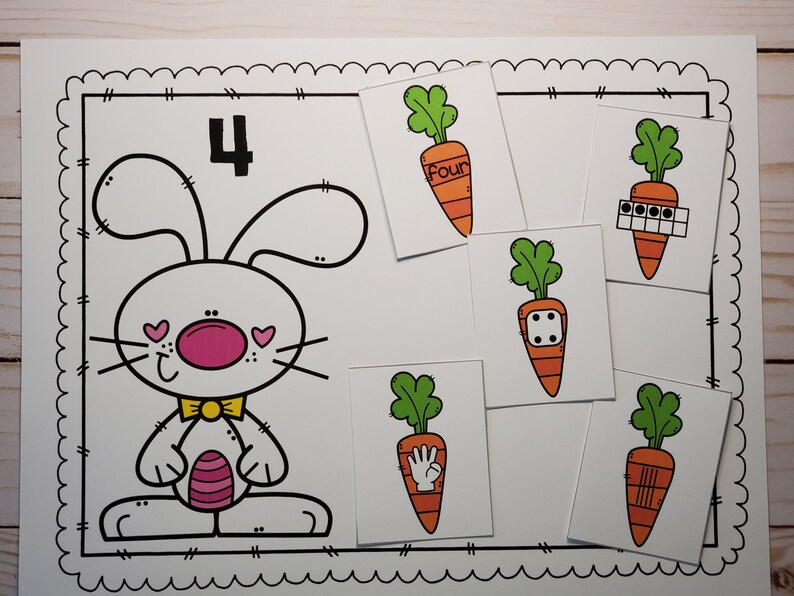 May include: A printable worksheet featuring a cartoon bunny with the number 4. There are five cards with carrots, each showing a different way to represent the number four: the word "four", four dots, a dice with four dots, a hand with four fingers, and four lines.
