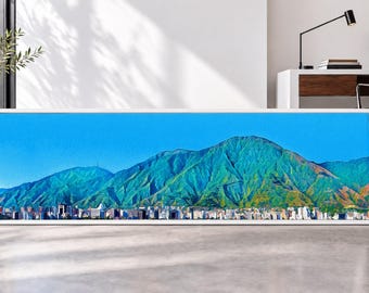 May include: A panoramic framed wall art print featuring a vibrant landscape of a city skyline nestled at the base of a massive, steep mountain range under a clear, bright blue sky. The mountain slopes display shades of green and brown.