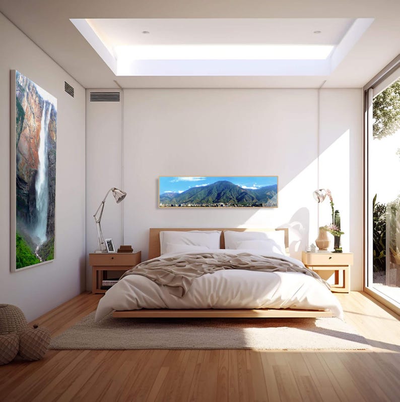 May include: A white bedroom with a large bed, a white duvet, and two bedside tables. There are two framed landscape photographs on the wall, one of a waterfall and one of a mountain range. The room has a skylight and a large window with a view of a garden.