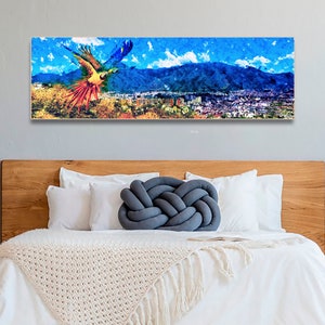 May include: A colorful painting of a parrot flying over a city with mountains in the background. The parrot is painted in shades of yellow, red, blue, and green. The city is painted in shades of gray and brown. The mountains are painted in shades of blue and purple.