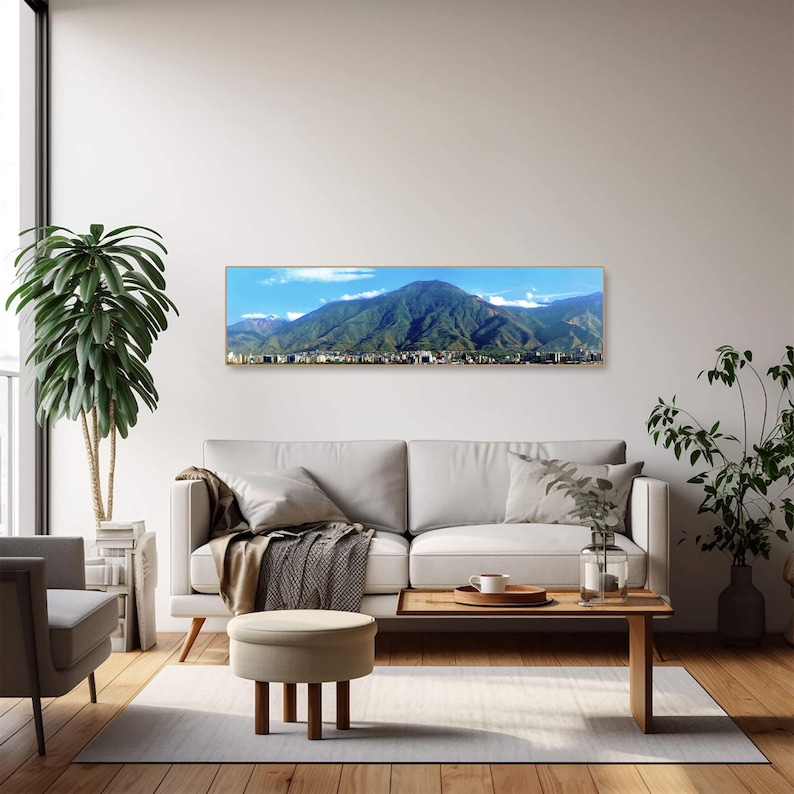 May include: A panoramic photograph of a mountain range with a city in the foreground. The mountain range is covered in green vegetation and the sky is blue with white clouds. The city is a blur of buildings and trees.