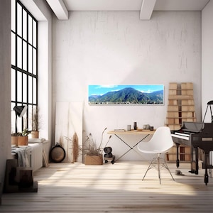 May include: A panoramic photograph of a mountain range with a city in the foreground. The photograph is framed and hanging on a white wall in a modern living room.