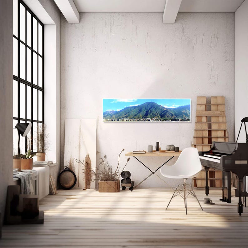 May include: A panoramic photograph of a mountain range with a city in the foreground. The photograph is framed and hanging on a white wall in a modern living room.