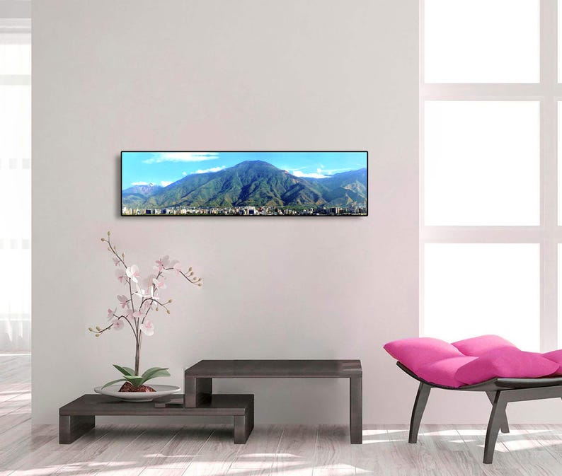May include: A panoramic photograph of a mountain range with a city in the foreground. The photo is framed in a black frame and is hanging on a white wall.